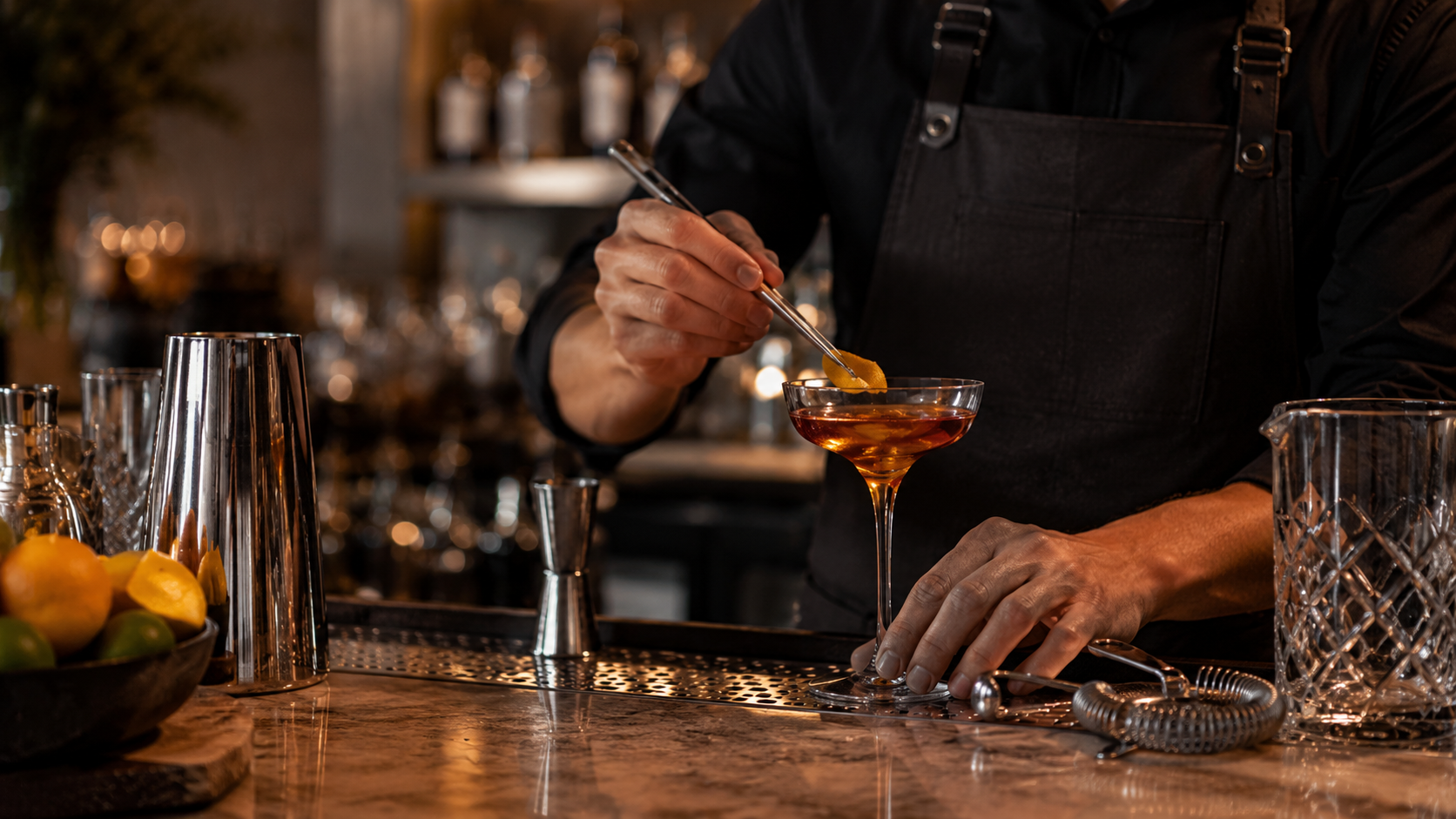 Bartender garnerar en cocktail i coupeglas med citrusskal